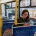 Jovem usando celular com fones em ônibus vazio durante o dia.