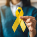 Pessoa segura laço amarelo simbolizando conscientização sobre prevenção ao suicídio.