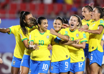 Jogadoras da seleção brasileira feminina de futebol comemoram gol abraçadas em campo, com a camisa amarela e o calção azul, em partida de Copa do Mundo Feminina.
