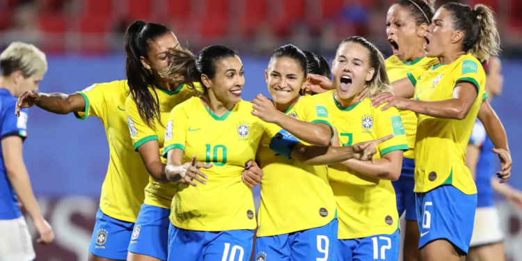 Jogadoras da seleção brasileira feminina de futebol comemoram gol abraçadas em campo, com a camisa amarela e o calção azul, em partida de Copa do Mundo Feminina.