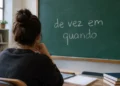 Jovem de costas, em ambiente de estudos, observa um quadro verde com a expressão “de vez em quando” escrita em giz.