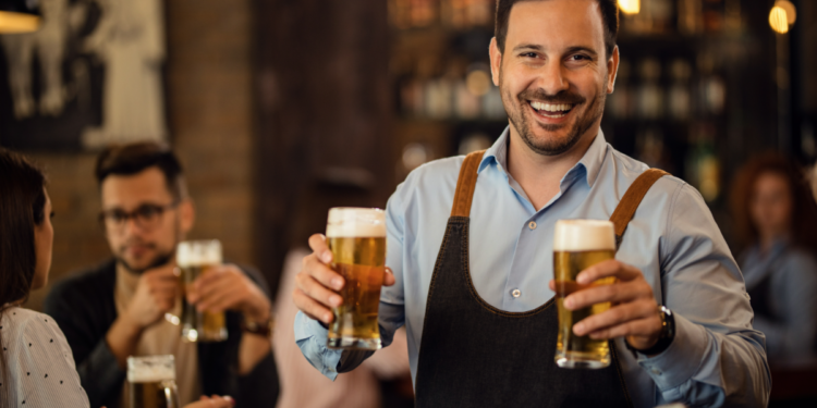 Homem sorridente segurando copos de cerveja em bar.