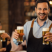 Homem sorridente segurando copos de cerveja em bar.