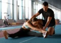 Profissional de Educação Física orientando alongamento de atleta em academia durante treinamento físico.