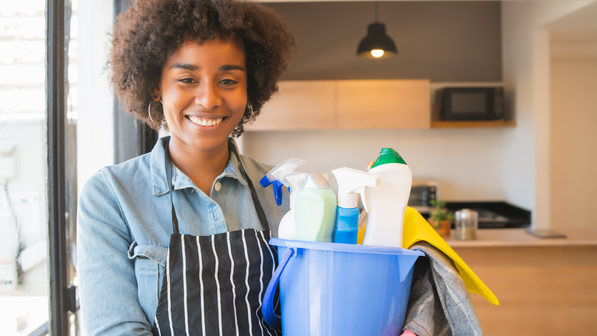 Profissional sorridente com produtos de limpeza em cozinha moderna.