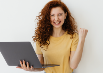 Jovem comemora vitória com notebook em fundo claro.