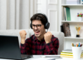 Jovem comemorando conquista online em ambiente de estudos.