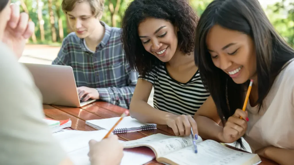 Alunos felizes sentados e estudando ao ar livre.