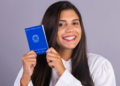 Jovem sorrindo exibe Carteira de Trabalho brasileira em fundo neutro.