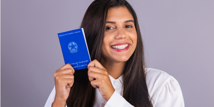 Jovem sorrindo exibe Carteira de Trabalho brasileira em fundo neutro.