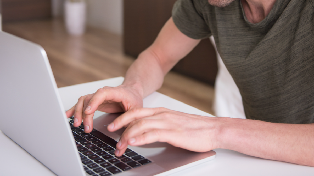 Jovem digitando em laptop prateado em ambiente residencial.
