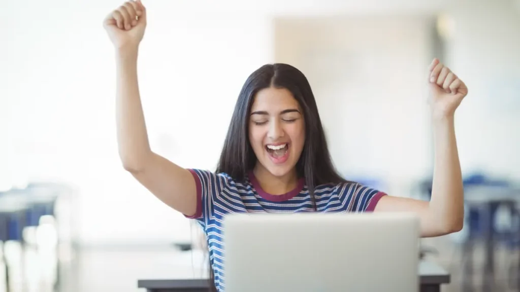 Jovem comemorando aprovação online com entusiasmo.