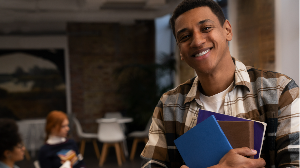 Jovem universitário sorridente com livros em biblioteca moderna.