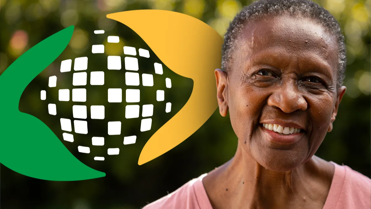 Idosa sorrindo ao lado da logo do INSS em ambiente externo.