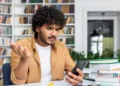 Estudante consulta o celular com expressão de dúvida sobre pagamento do Pé-de-Meia de agosto.