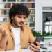 Estudante consulta o celular com expressão de dúvida sobre pagamento do Pé-de-Meia de agosto.