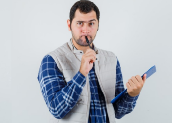 Homem segurando prancheta e caneta com expressão pensativa sobre fundo branco.