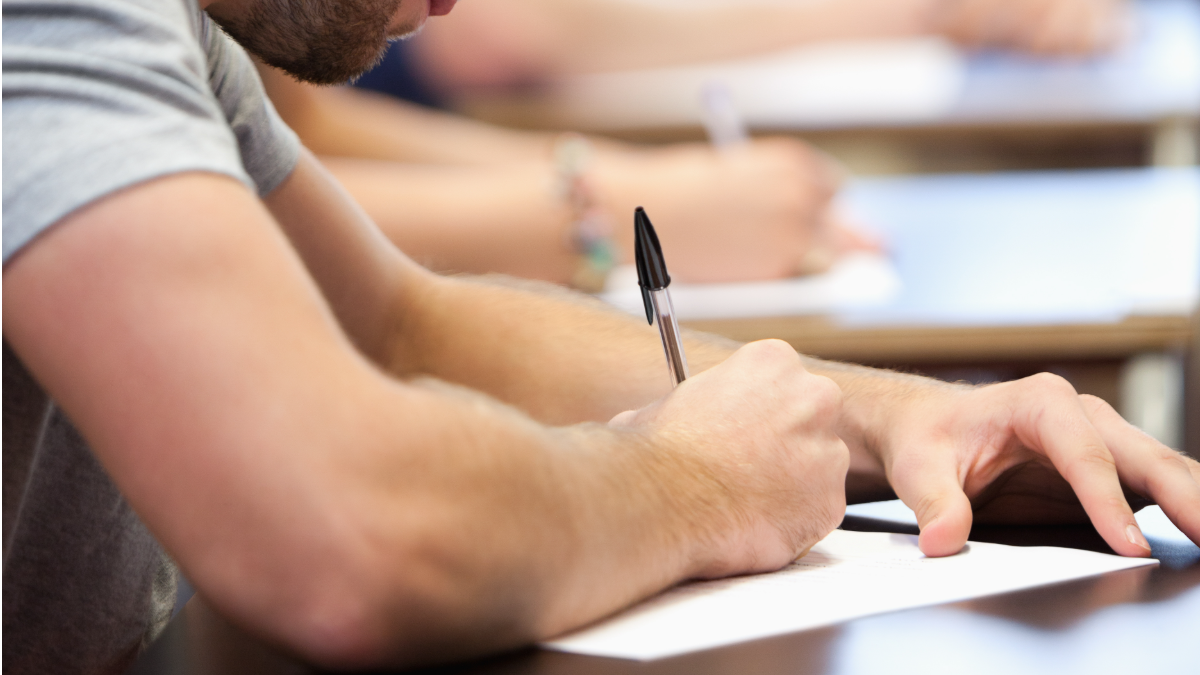 Jovem escrevendo prova em sala de aula durante exame.
