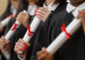 Pessoas segurando diplomas com laços vermelhos.