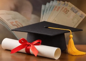 Capelo de formatura e diploma ao lado de notas de dinheiro representam aumento salarial após a graduação.