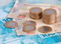 Dinheiro brasileiro em foco com notas de 50 e 100 reais e moedas.