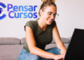Mulher mexendo em notebook ao lado da logo da Pensar Cursos.