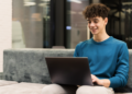 Jovem sorrindo usando notebook em ambiente moderno.