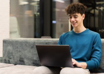 Jovem sorrindo usando notebook em ambiente moderno.