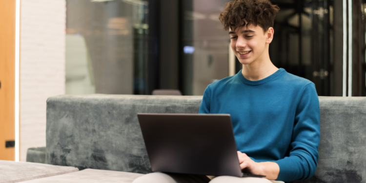 Jovem sorrindo usando notebook em ambiente moderno.