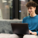 Jovem sorrindo usando notebook em ambiente moderno.