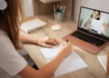 Aula online com aluna escrevendo em caderno.