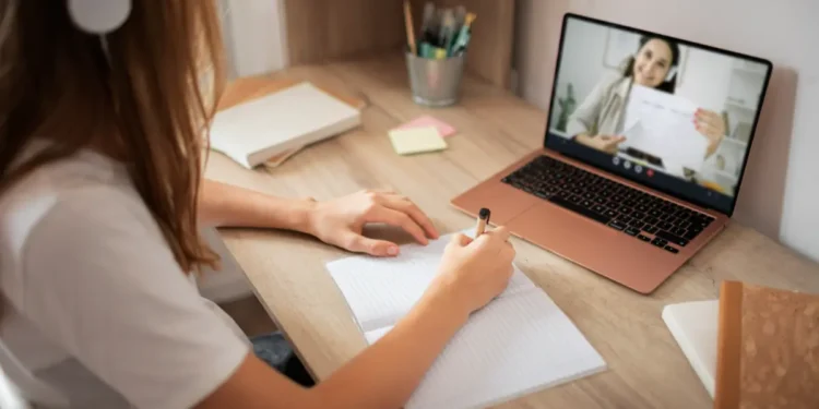 Aula online com aluna escrevendo em caderno.