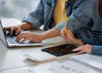 Duas pessoas trabalhando com notebook e anotações encima da mesa.