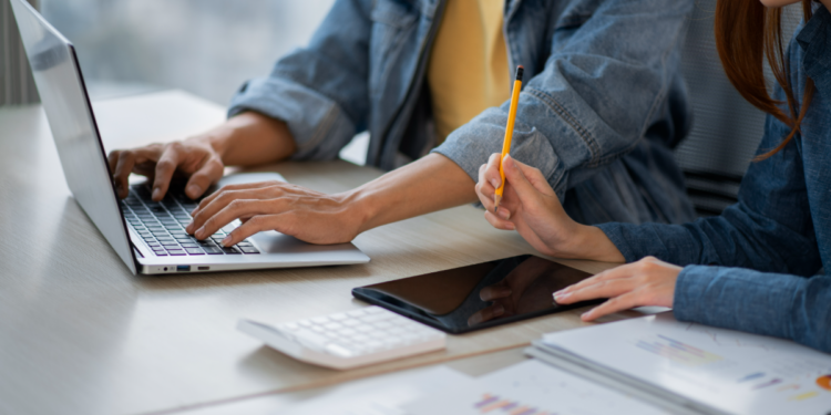 Duas pessoas trabalhando com notebook e anotações encima da mesa.