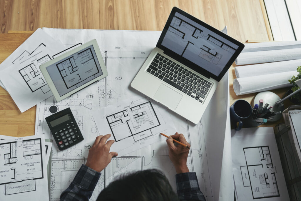 Imagem ilustrativa: plantas impressas, tablet e notebook com projeto arquitetônico, sobre o AutoCAD grátis para estudante