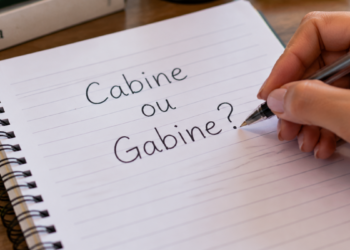 Mão escrevendo em caderno a dúvida entre cabine e gabine na língua portuguesa.
