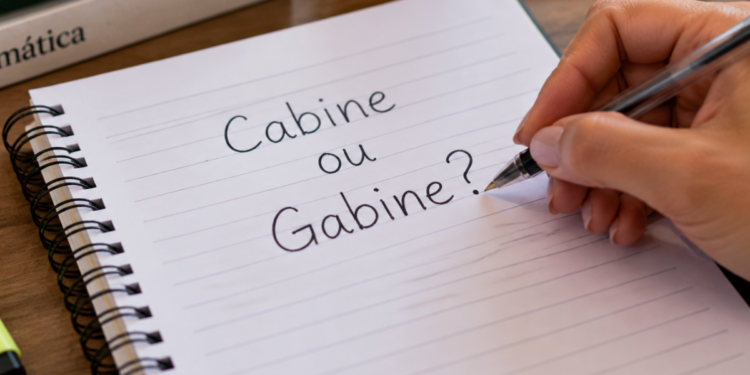 Mão escrevendo em caderno a dúvida entre cabine e gabine na língua portuguesa.