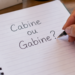 Mão escrevendo em caderno a dúvida entre cabine e gabine na língua portuguesa.