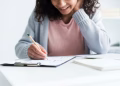 Imagem ilustrativa de estudante sorridente fazendo anotações em uma prancheta com gráficos, em preparação para o concurso IBGE