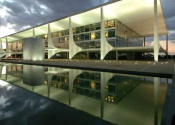 Fachada iluminada do Palácio do Planalto refletida no espelho d'água ao entardecer, sede do governo brasileiro em Brasília.