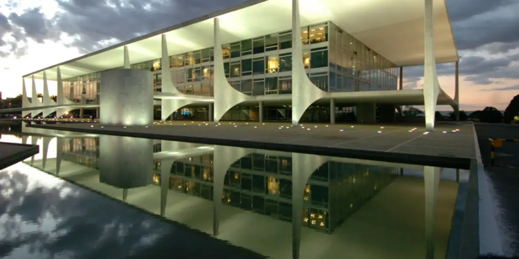 Fachada iluminada do Palácio do Planalto refletida no espelho d'água ao entardecer, sede do governo brasileiro em Brasília.