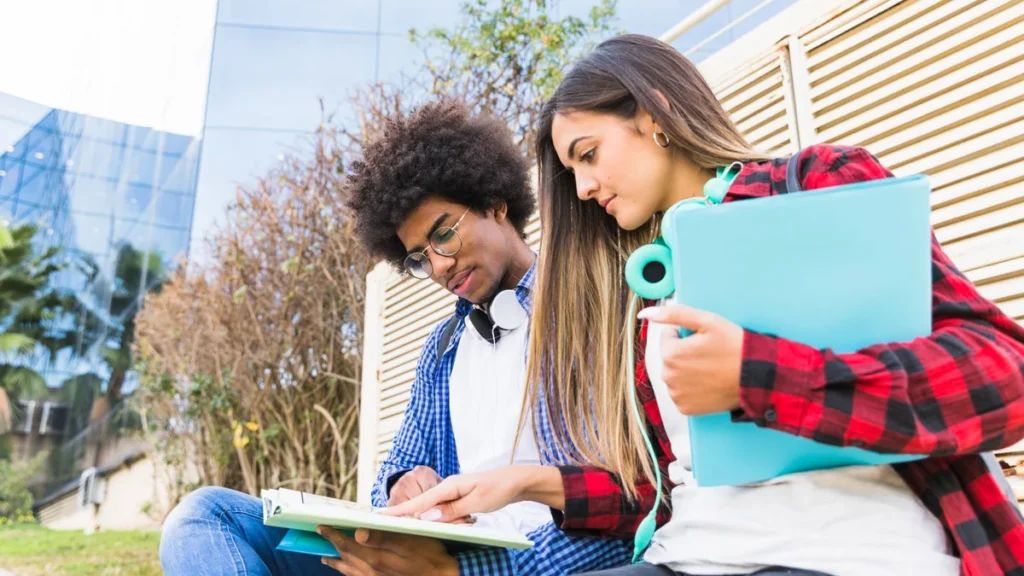 Dois estudantes analisam materiais acadêmicos em frente a uma universidade, representando fatores que influenciam a remuneração após a formação.