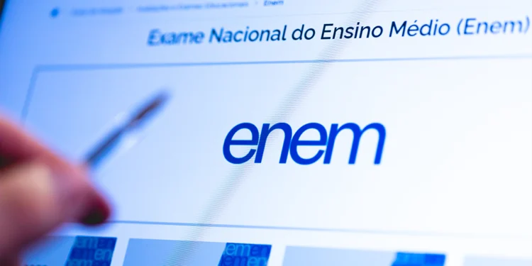 Tela de computador exibindo site do Enem com logo e mão segurando caneta à esquerda, simbolizando o processo de download da cartilha do Enem 2026.