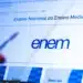 Tela de computador exibindo site do Enem com logo e mão segurando caneta à esquerda, simbolizando o processo de download da cartilha do Enem 2026.