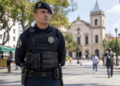 Guarda municipal de uniforme tático preto em praça urbana com igreja colonial ao fundo, simbolizando o concurso Guarda de Guarulhos.