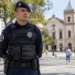 Guarda municipal de uniforme tático preto em praça urbana com igreja colonial ao fundo, simbolizando o concurso Guarda de Guarulhos.