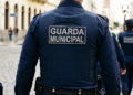 Guarda Municipal de costas com uniforme azul e patch, patrulhando rua de paralelepípedos em grupo, simbolizando o concurso em Caldas Novas/GO.