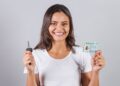 Mulher sorridente mostra CNH brasileira e chave de carro sobre fundo cinza claro, simbolizando os concursos que possuem exigência de CNH.