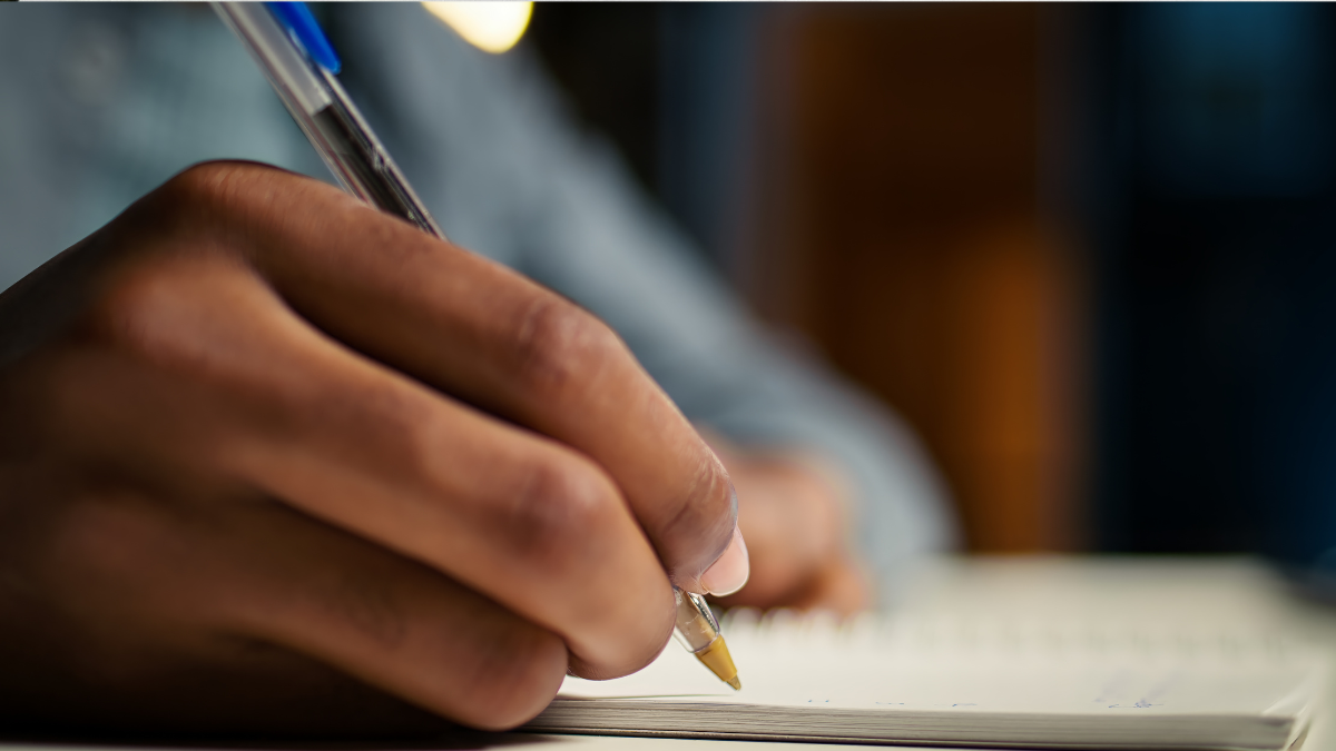 Pessoa escrevendo em caderno durante preparação para prova de concurso público da Câmara de Dois Córregos.