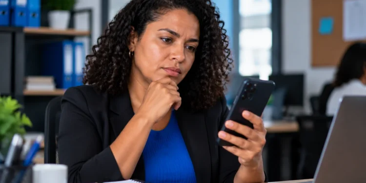 Mulher consultando informações sobre o 13º salário CLT pelo celular em ambiente de trabalho